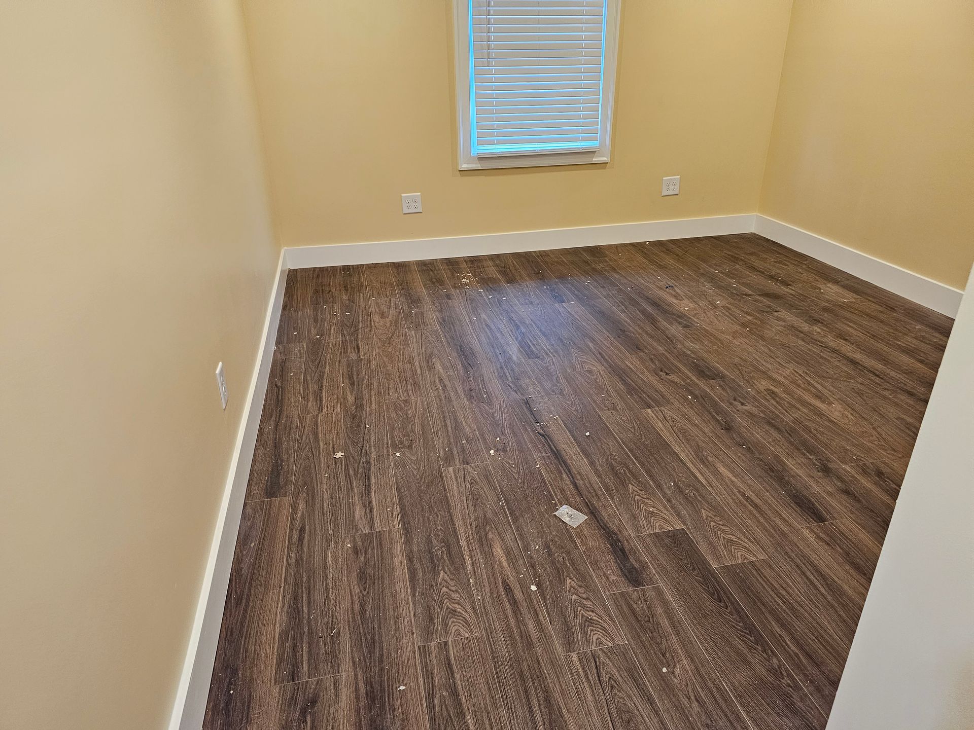 Empty beige room with wood flooring and a small window on the far wall