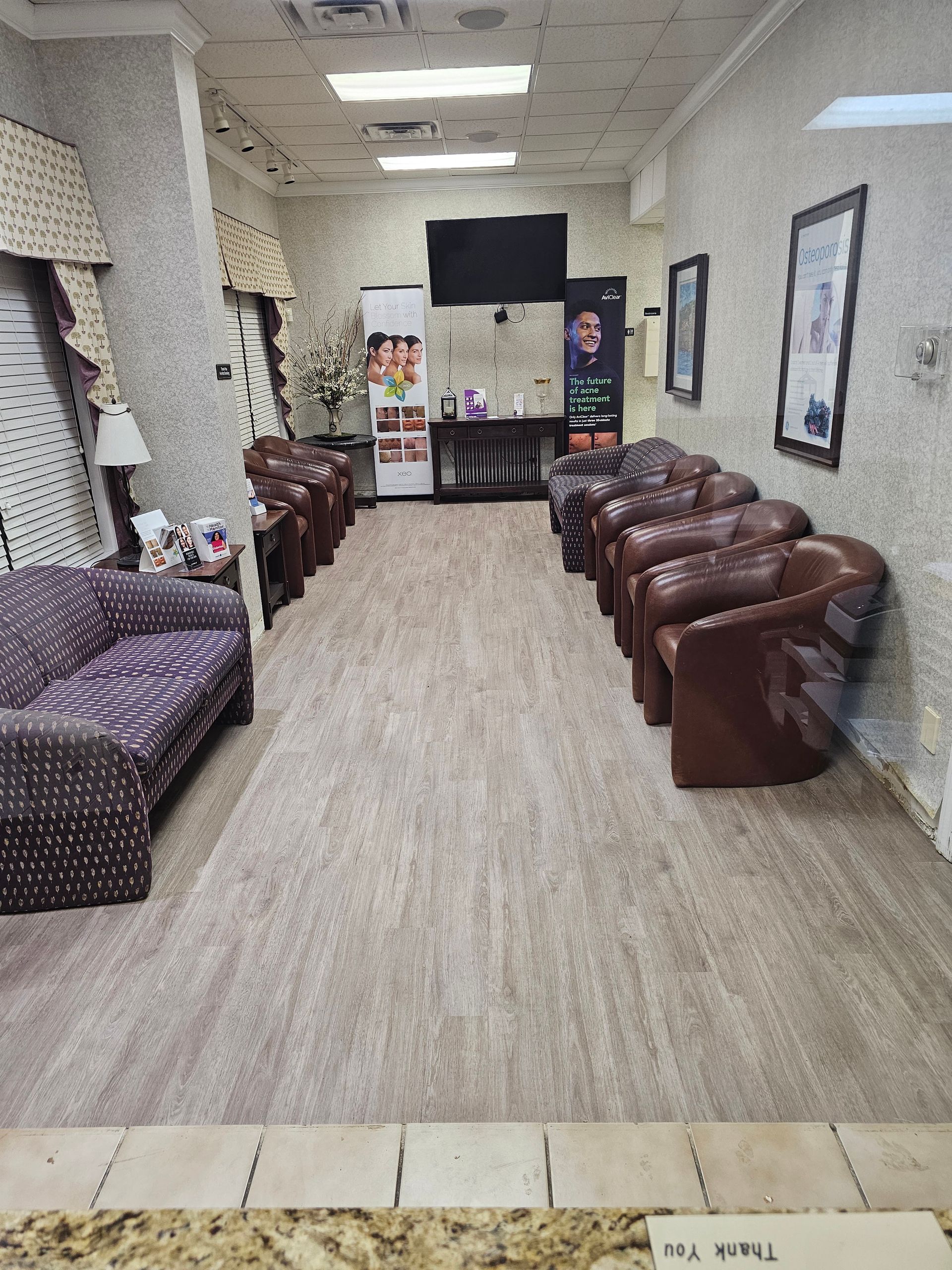 Empty waiting room with brown leather chairs, patterned sofas, and a TV on the far wall.