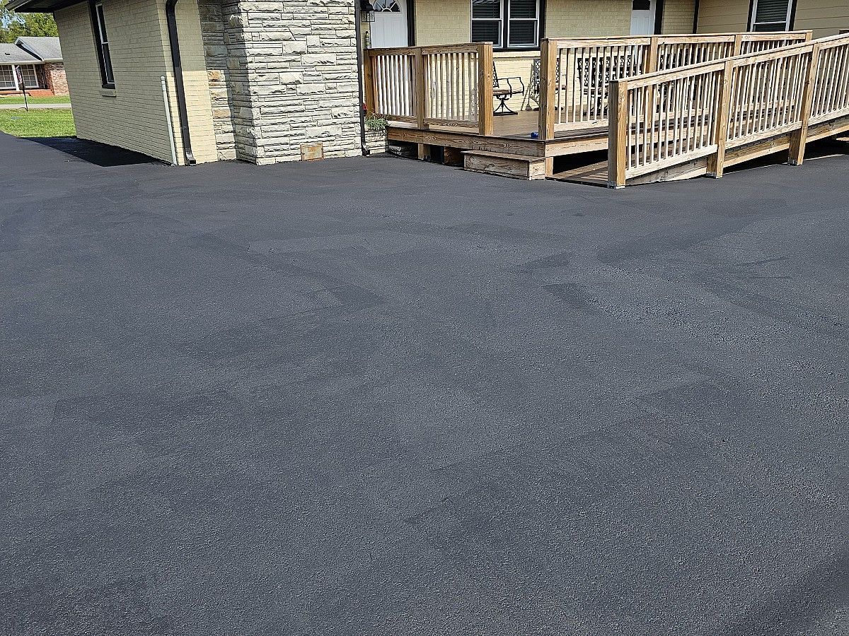 Fresh black asphalt driveway beside a house and wooden deck with railings