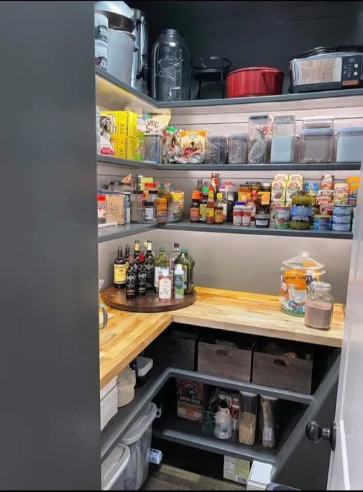Pantry with wooden shelves and countertops stocked with jars, cans, spices, and kitchen supplies.