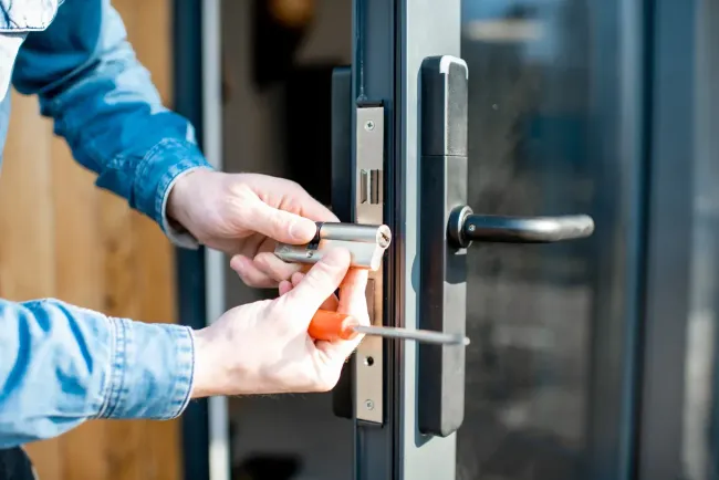 Hands using a screwdriver to adjust a door lock on a glass entrance door