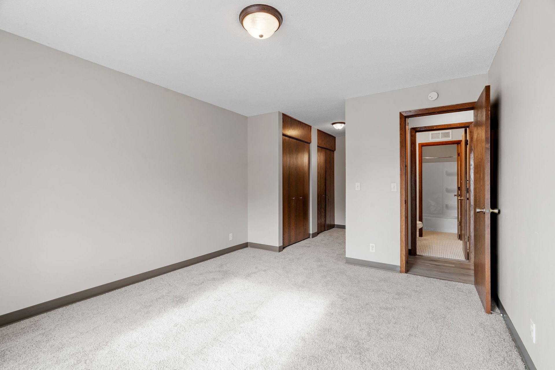 An empty bedroom with a carpeted floor and a door leading to a bathroom.