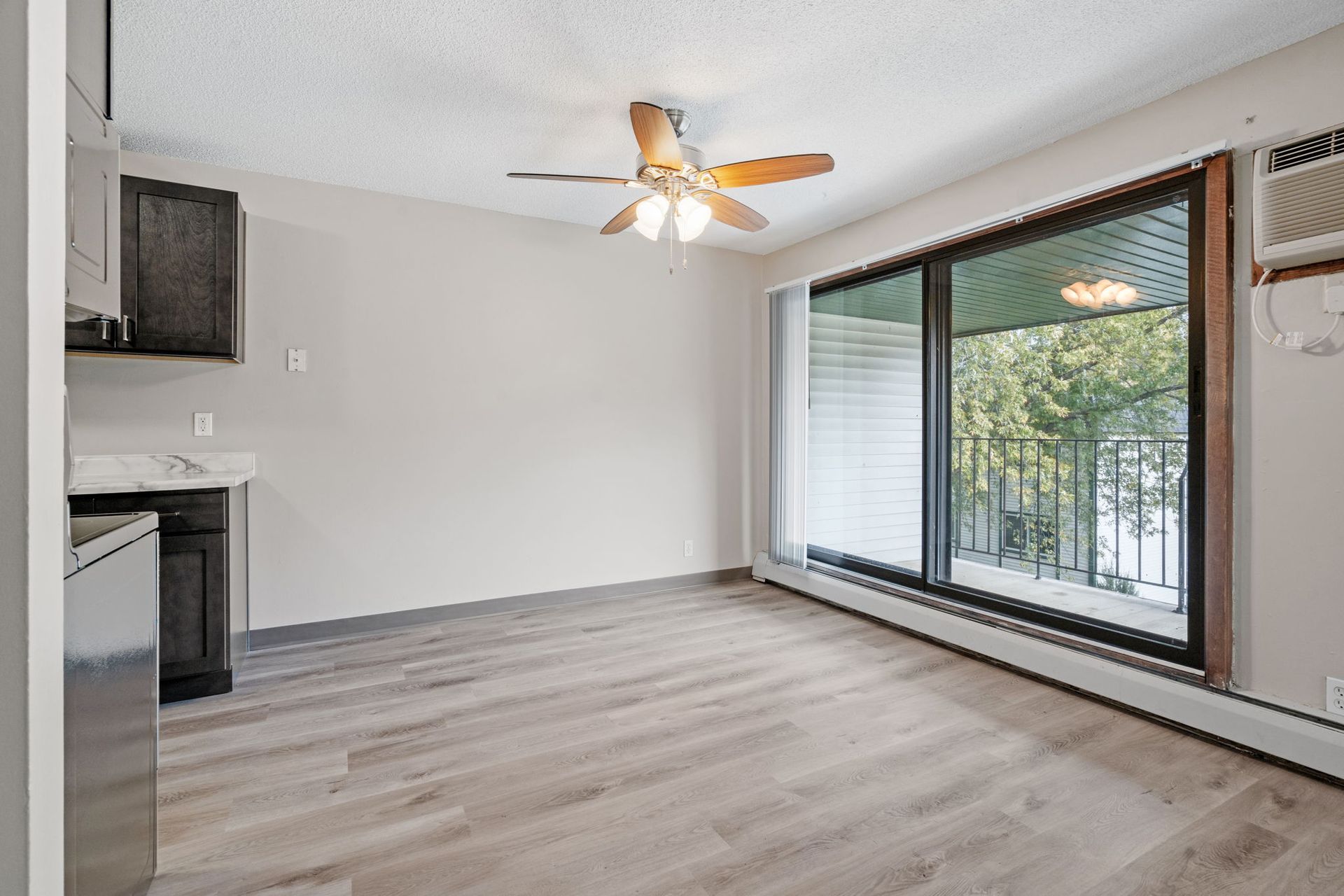 An empty living room with a ceiling fan and sliding glass doors leading to a balcony.