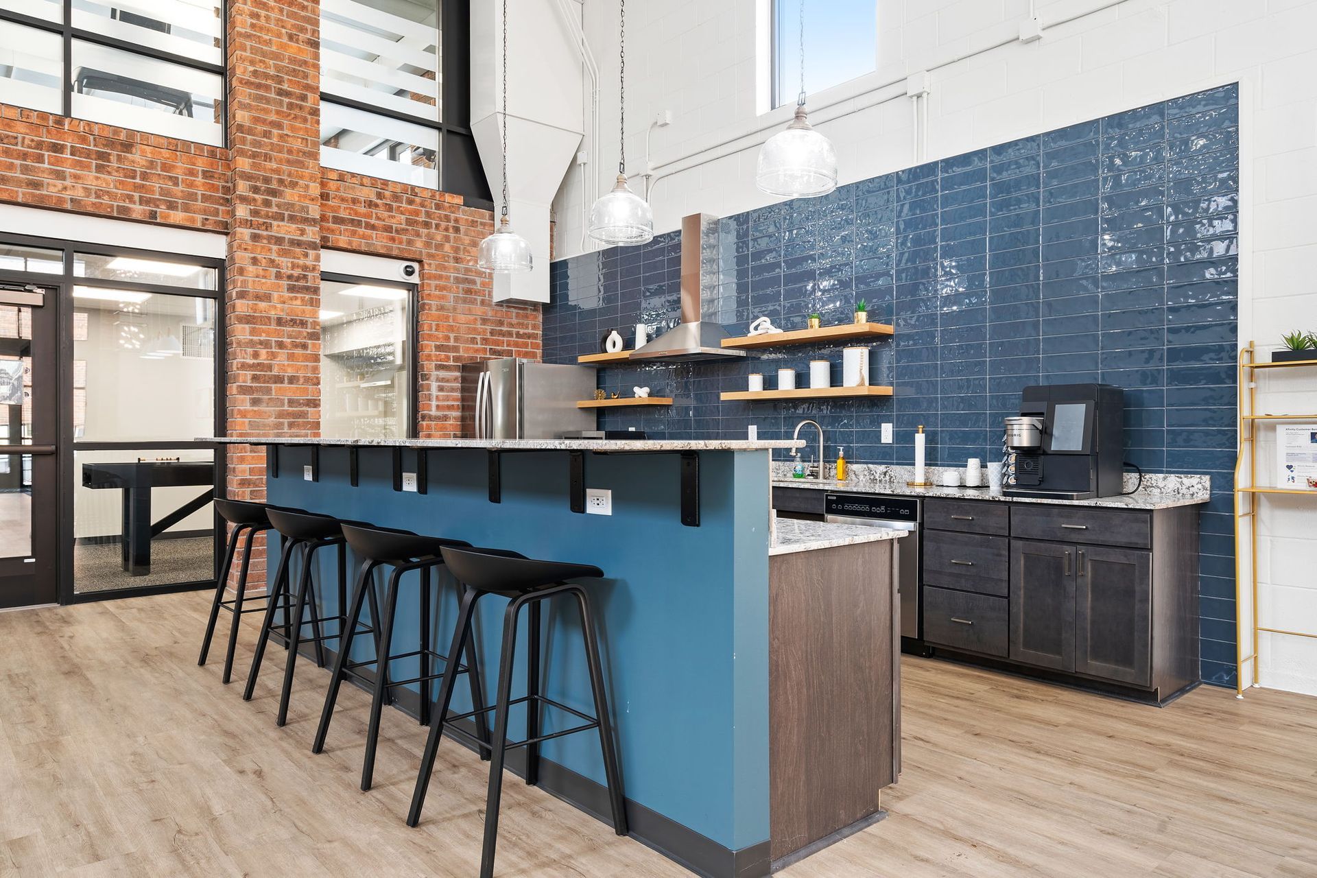 A kitchen with a blue island and stools and a brick wall.