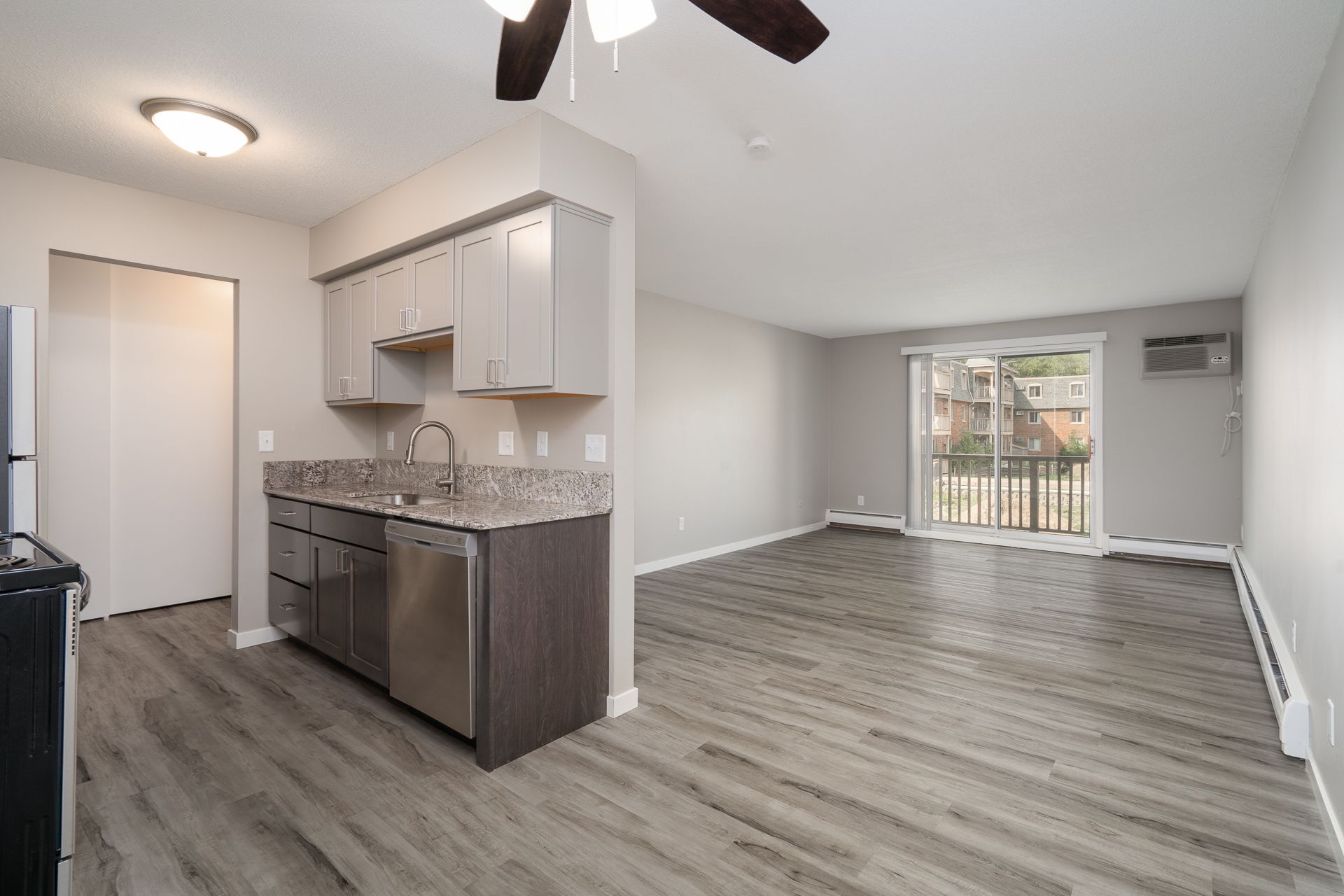 A living room with a ceiling fan and a kitchen with stainless steel appliances.