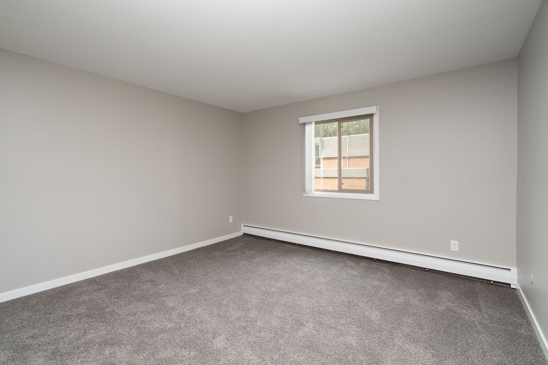 An empty living room with a window and a gray carpet.