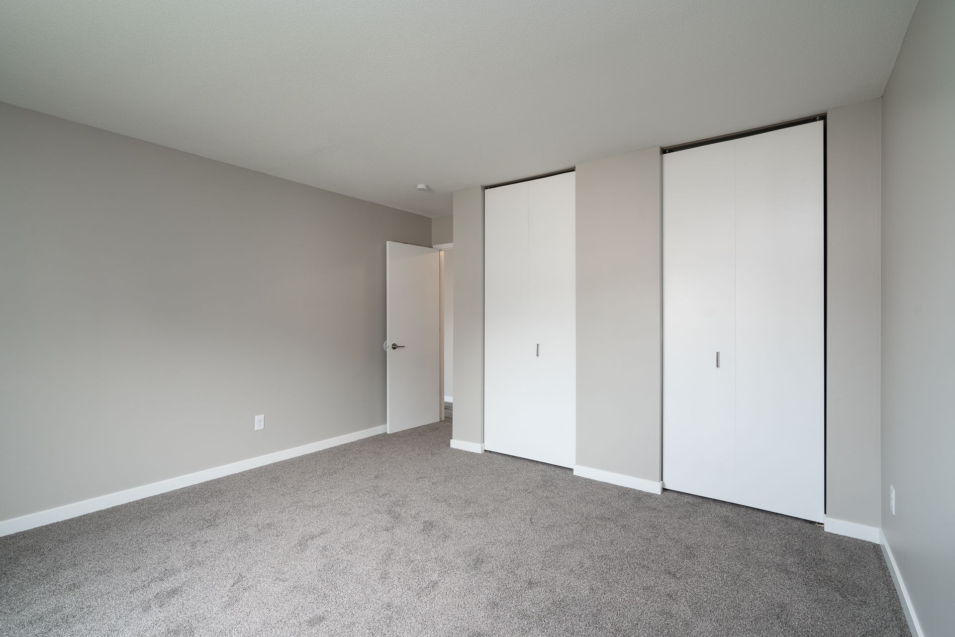 An empty bedroom with a carpeted floor and two closets.