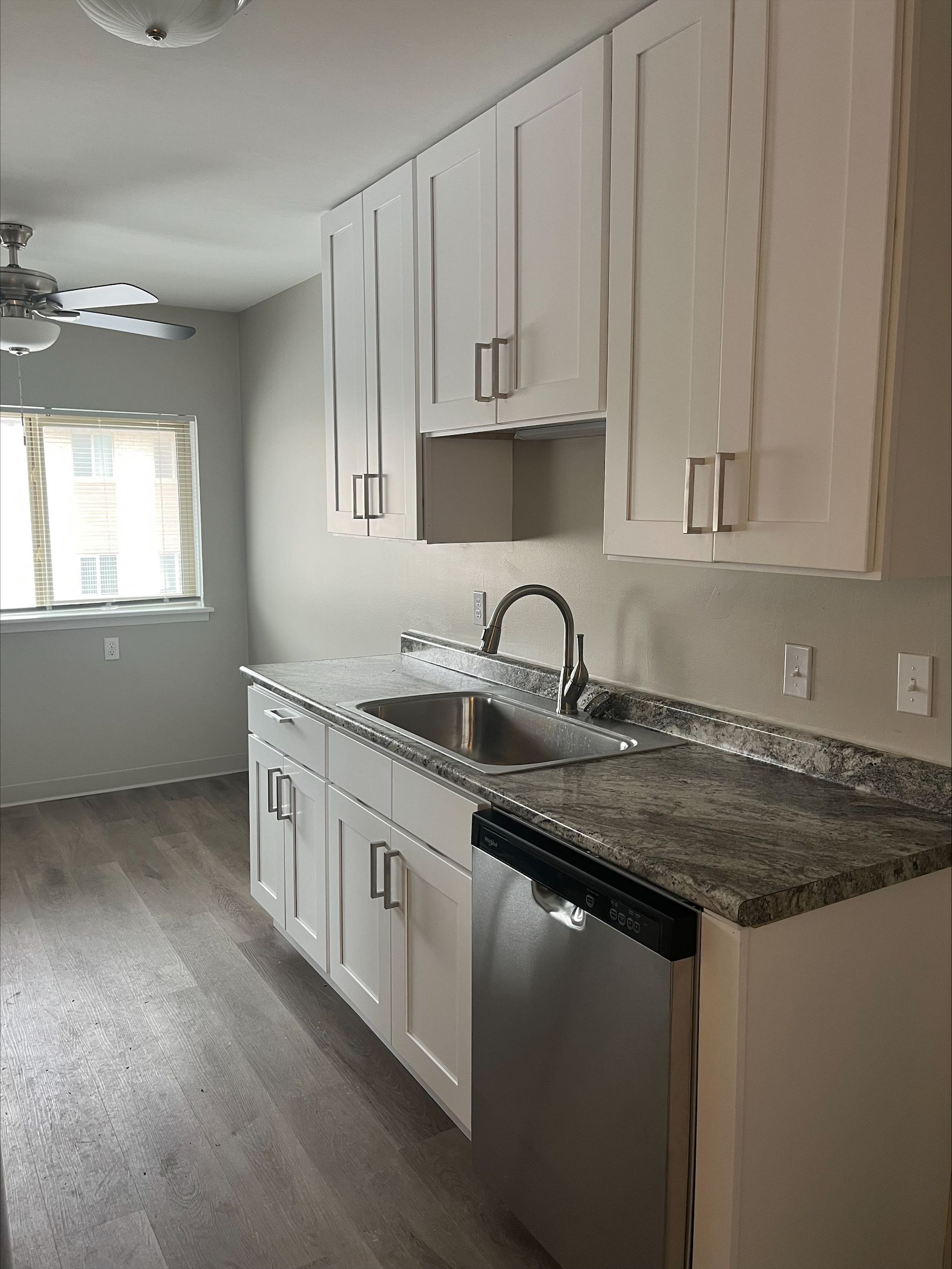 A kitchen with white cabinets , granite counter tops , a sink and a dishwasher.