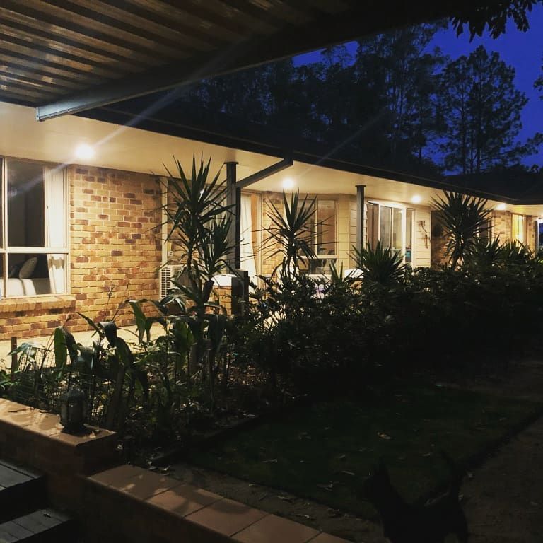 Dimly lit brick house porch with warm lights, potted plants, and a dark front yard at dusk