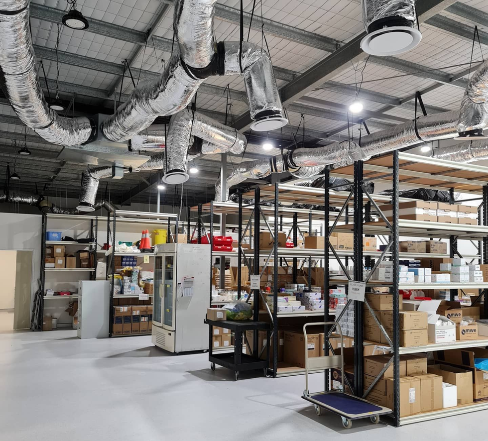 Warehouse interior with shelves, boxes, and exposed ductwork under bright industrial lighting