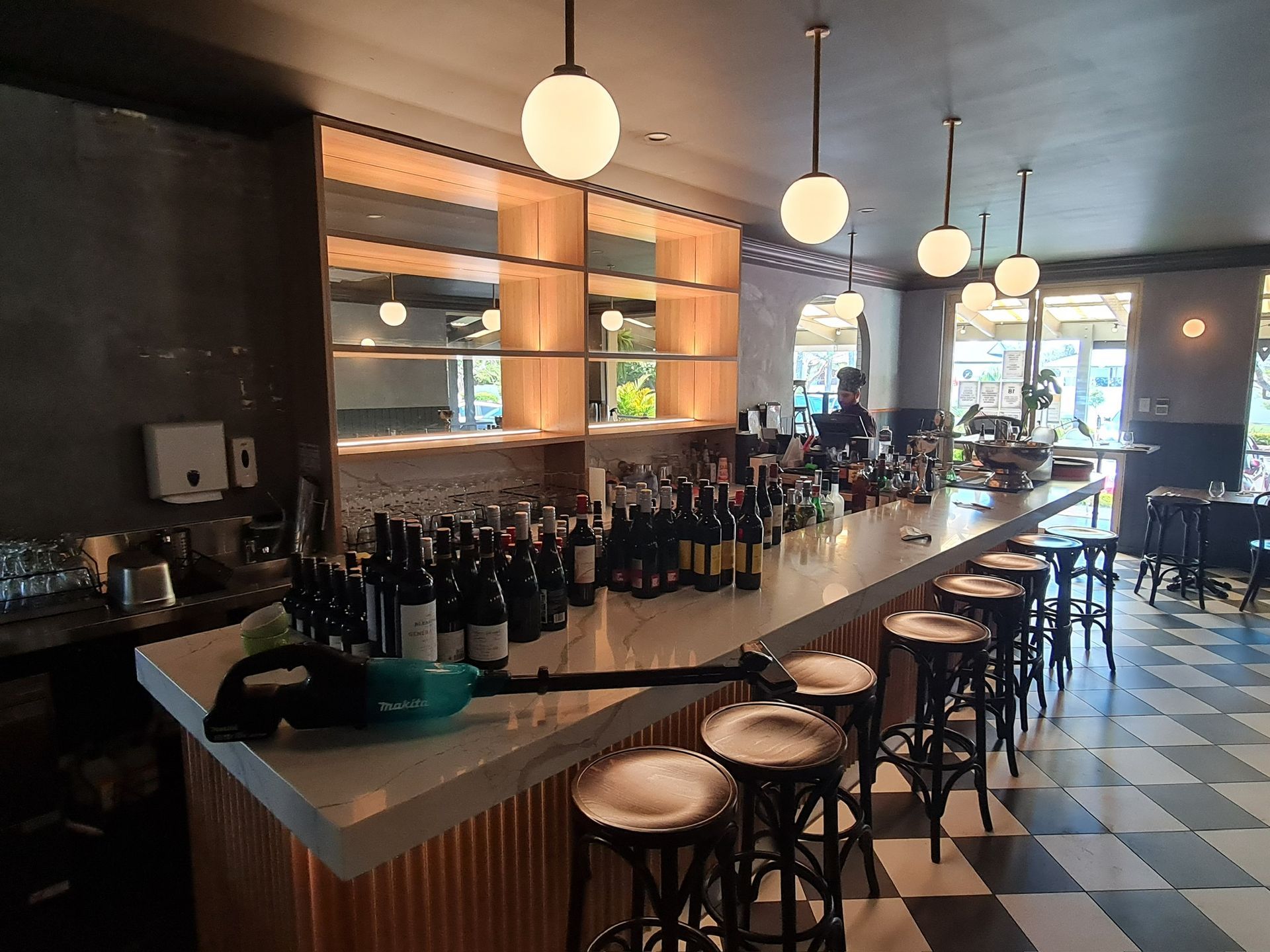 Modern bar interior with rows of wine bottles, hanging globe lights, and stools along a counter