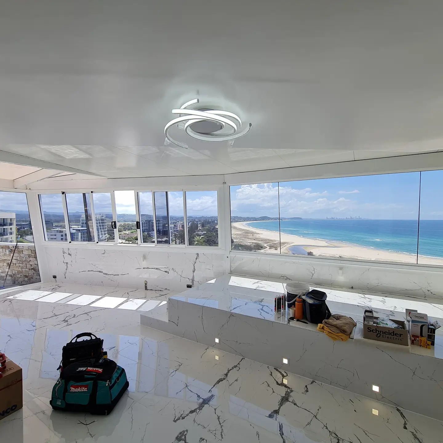 Modern white room with panoramic ocean view and scattered bags on the floor.