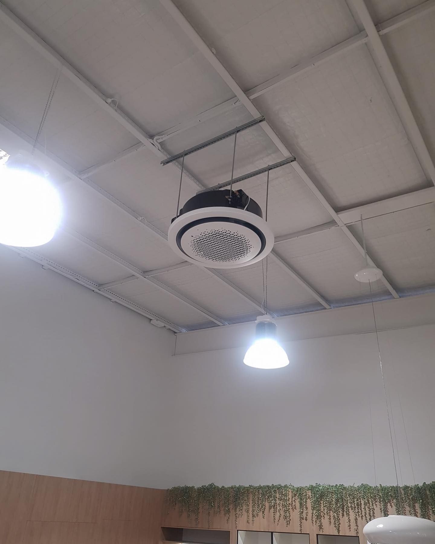 Ceiling-mounted round camera or speaker in a white room with hanging lights and wood paneling.