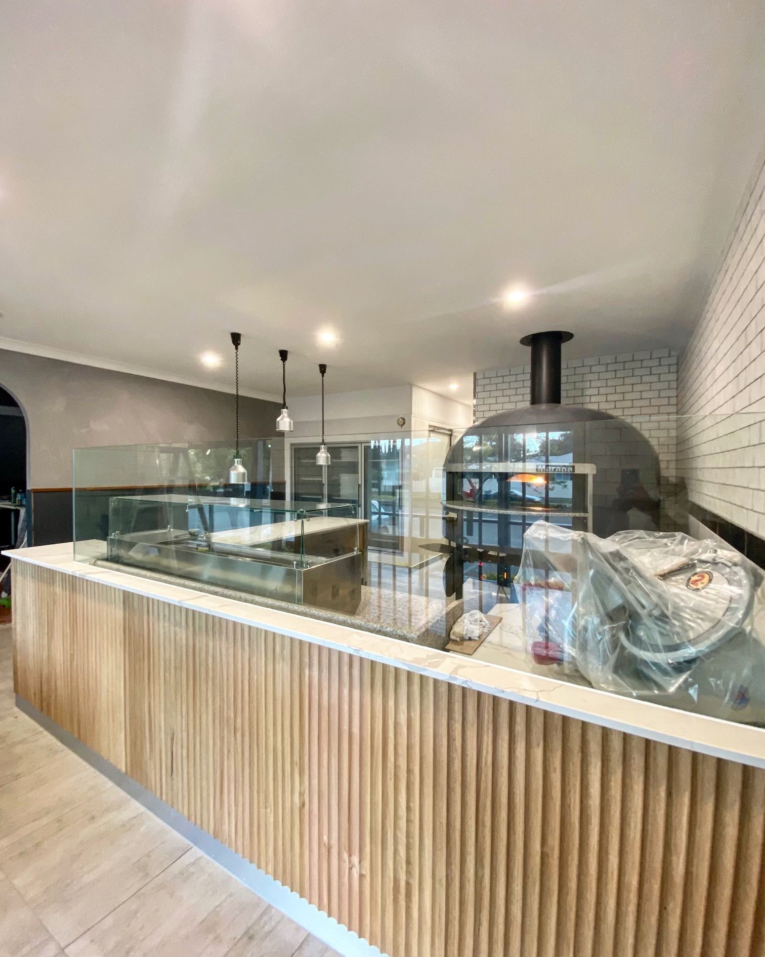 Modern bakery counter with glass display cases, wood slat front, and a brick pizza oven