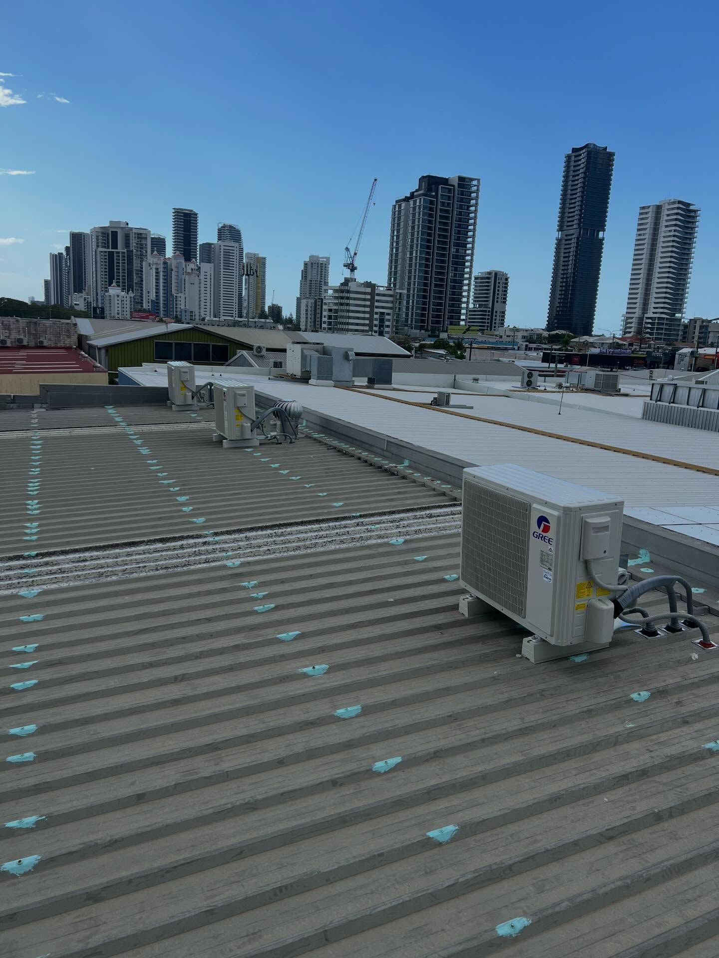 Rooftop HVAC units in foreground with a city skyline of tall apartment towers under a clear blue sky.