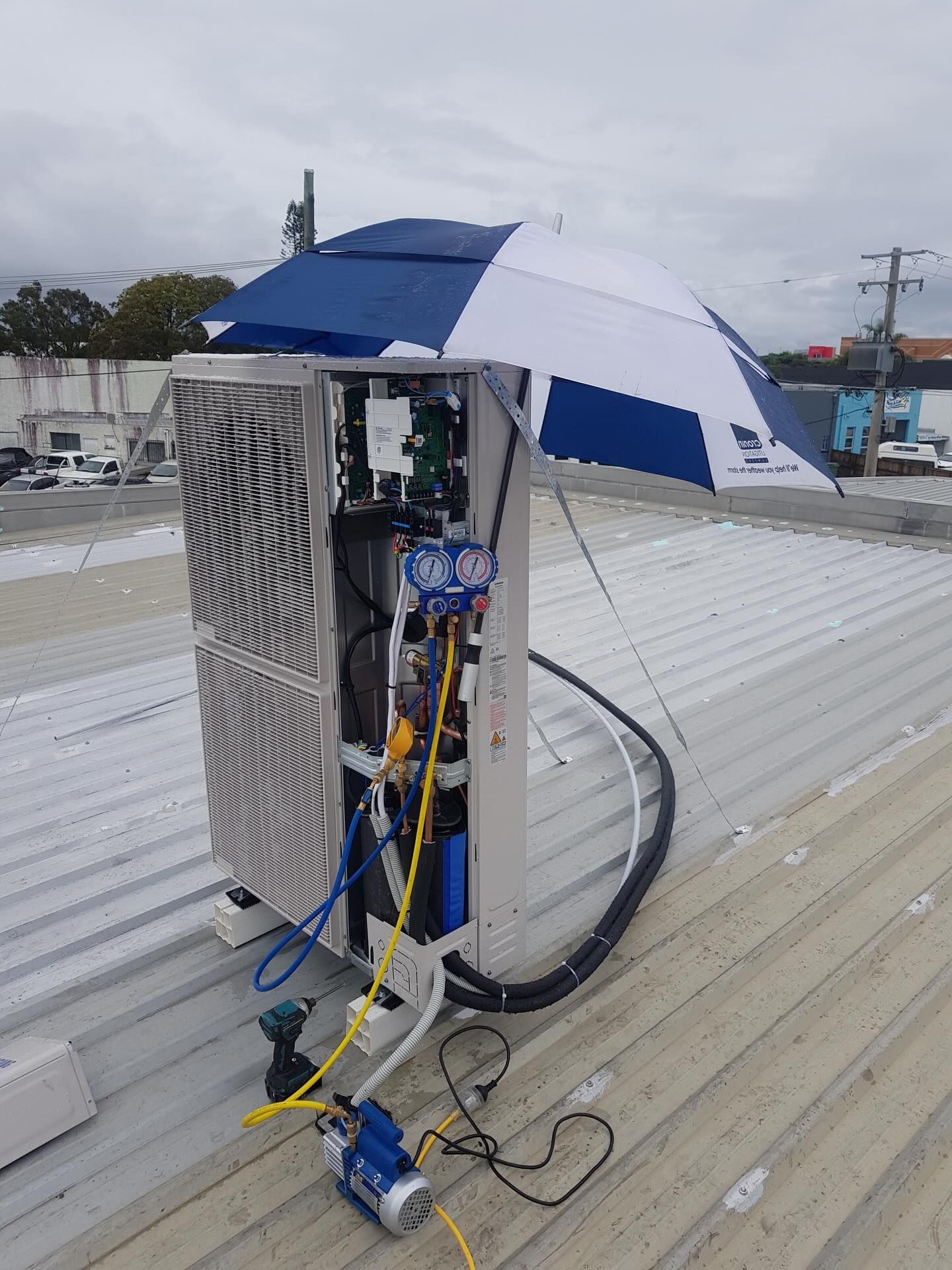 Blue-and-white umbrella shielding rooftop HVAC unit and exposed cables on a wet roof