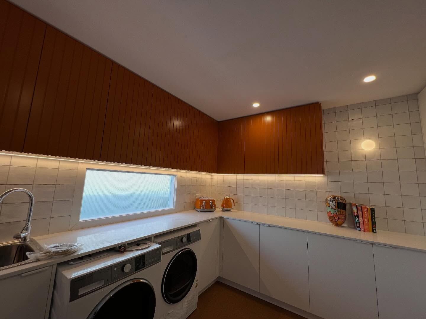 Modern kitchen with white cabinets, wood-paneled wall, tiled backsplash, and washer-dryer under the counter