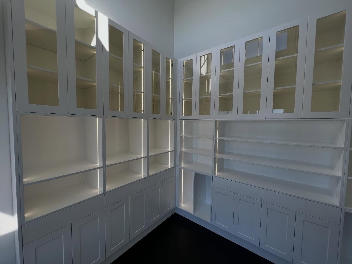 Empty white built-in cabinets lining a corner room, with glass-front upper doors and closed lower cabinets.