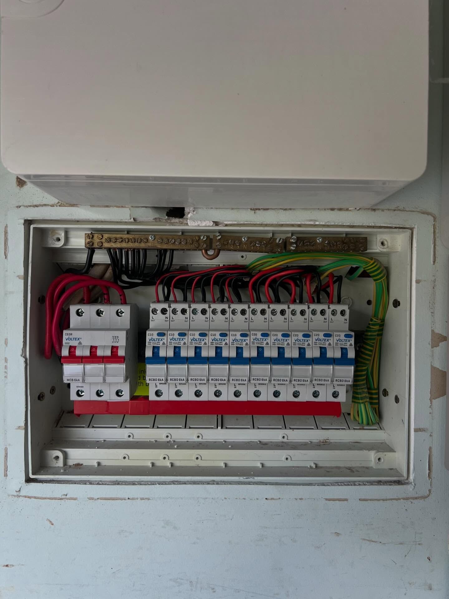 Open electrical breaker panel with rows of white circuit breakers and red wiring in a wall cabinet