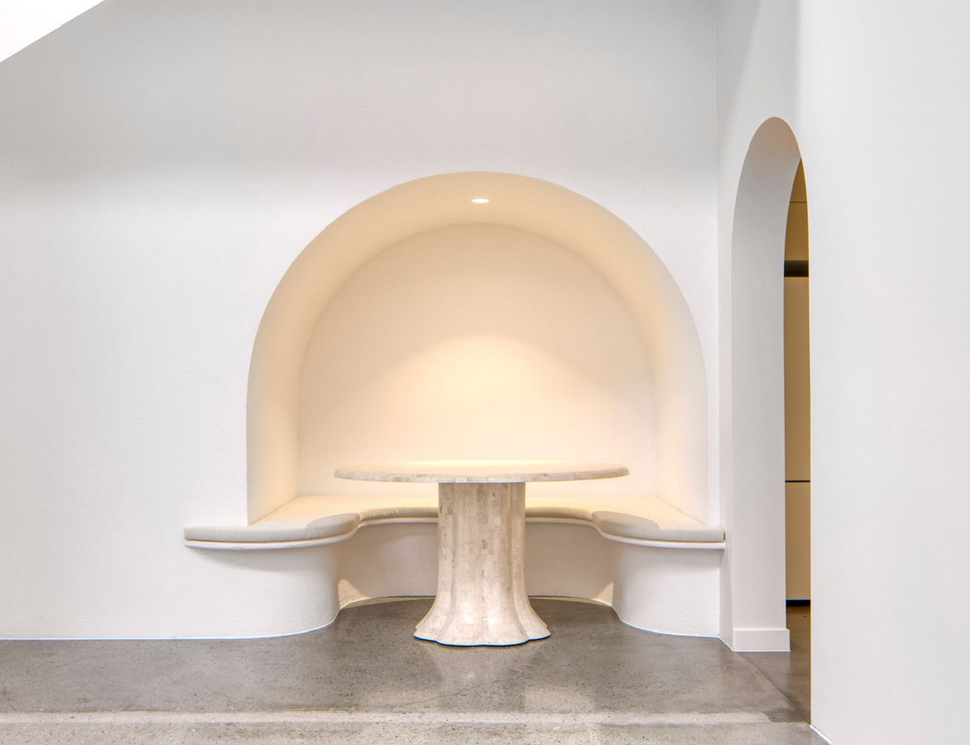 Minimalist white alcove seating area with a round pedestal table and built-in benches