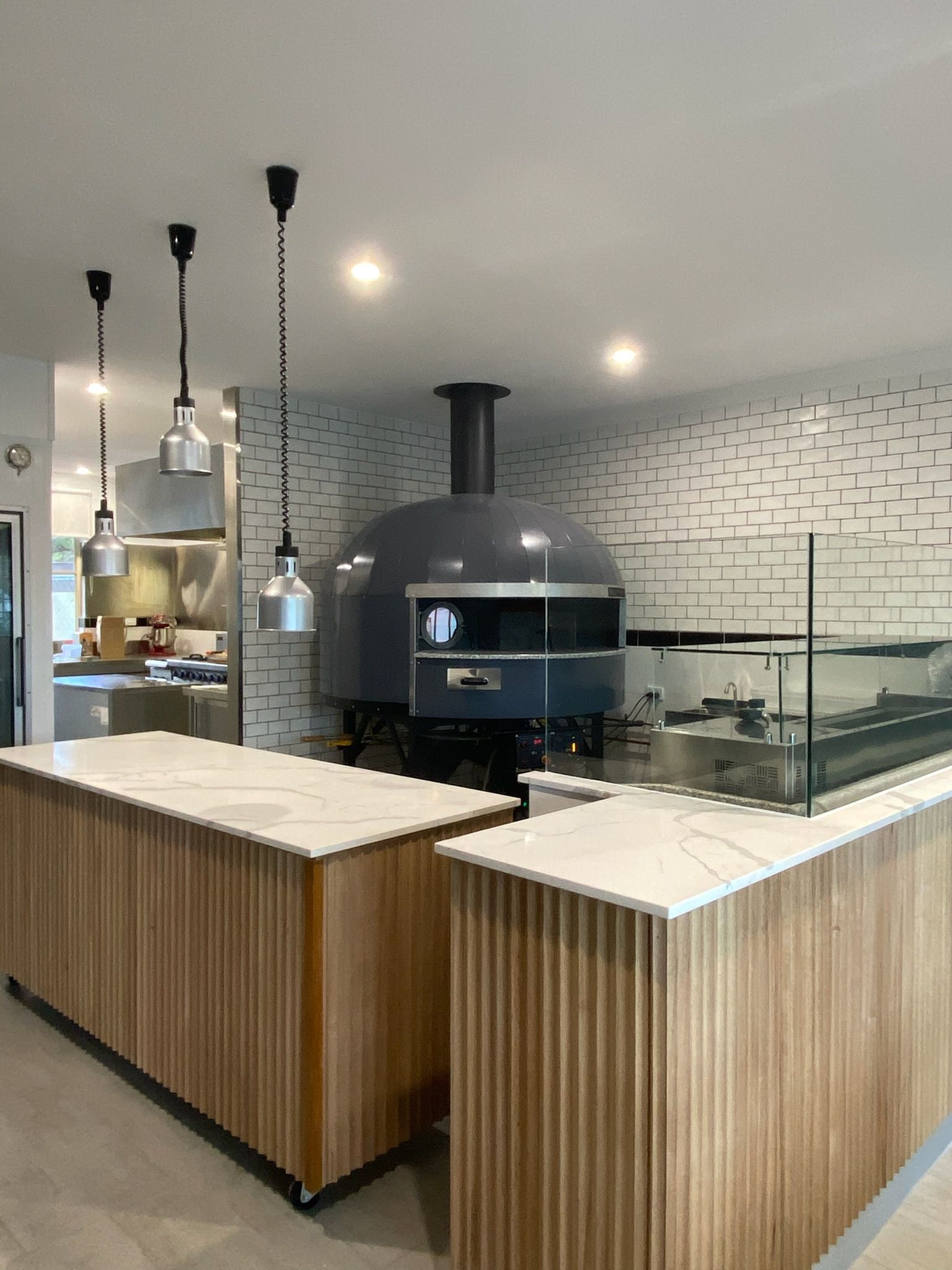 Modern pizza counter with wood panels, black oven, pendant lights, and tiled walls in a restaurant.