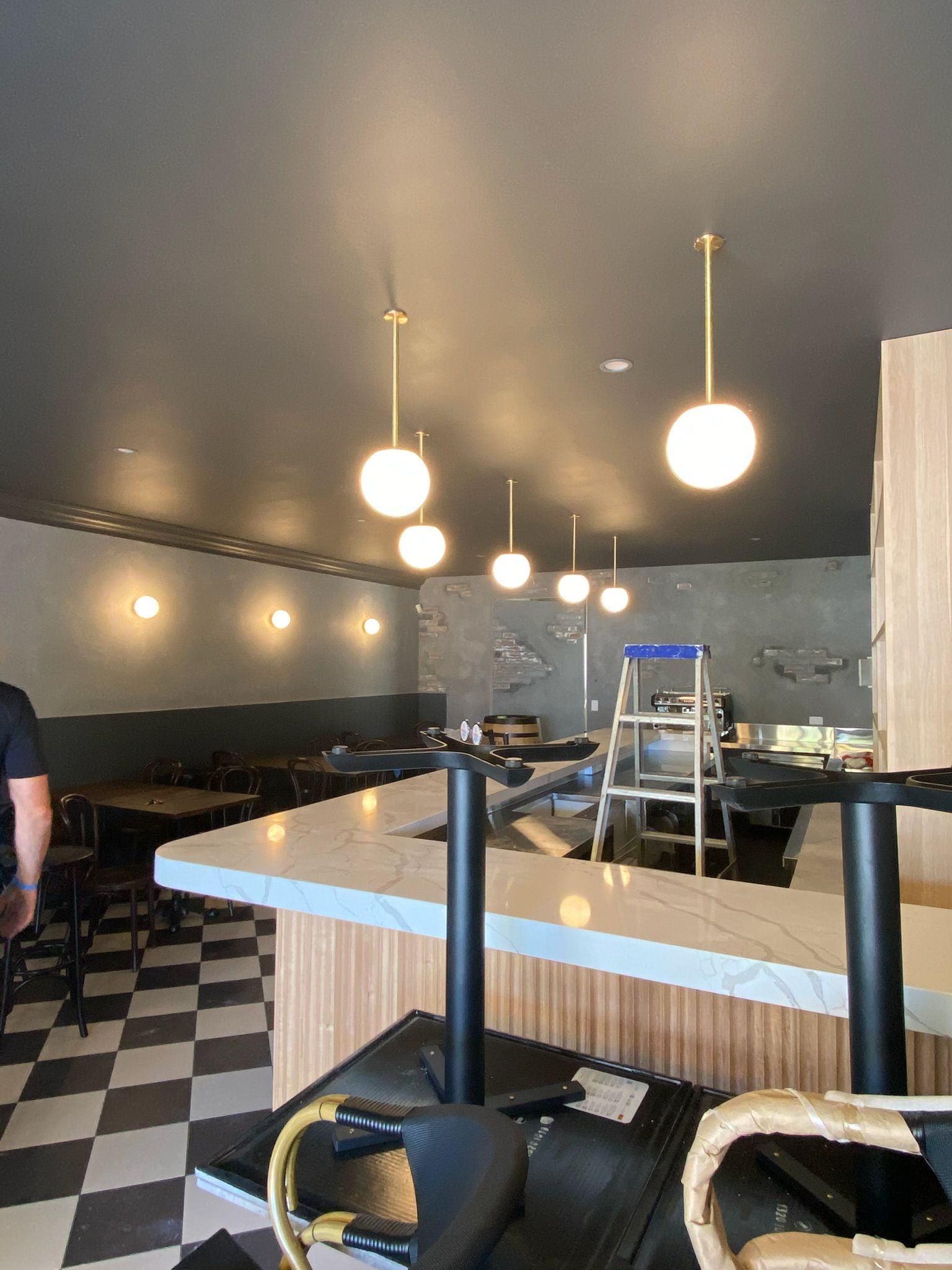 Empty restaurant interior with checkered floor, hanging globe lights, and a central counter with stools.