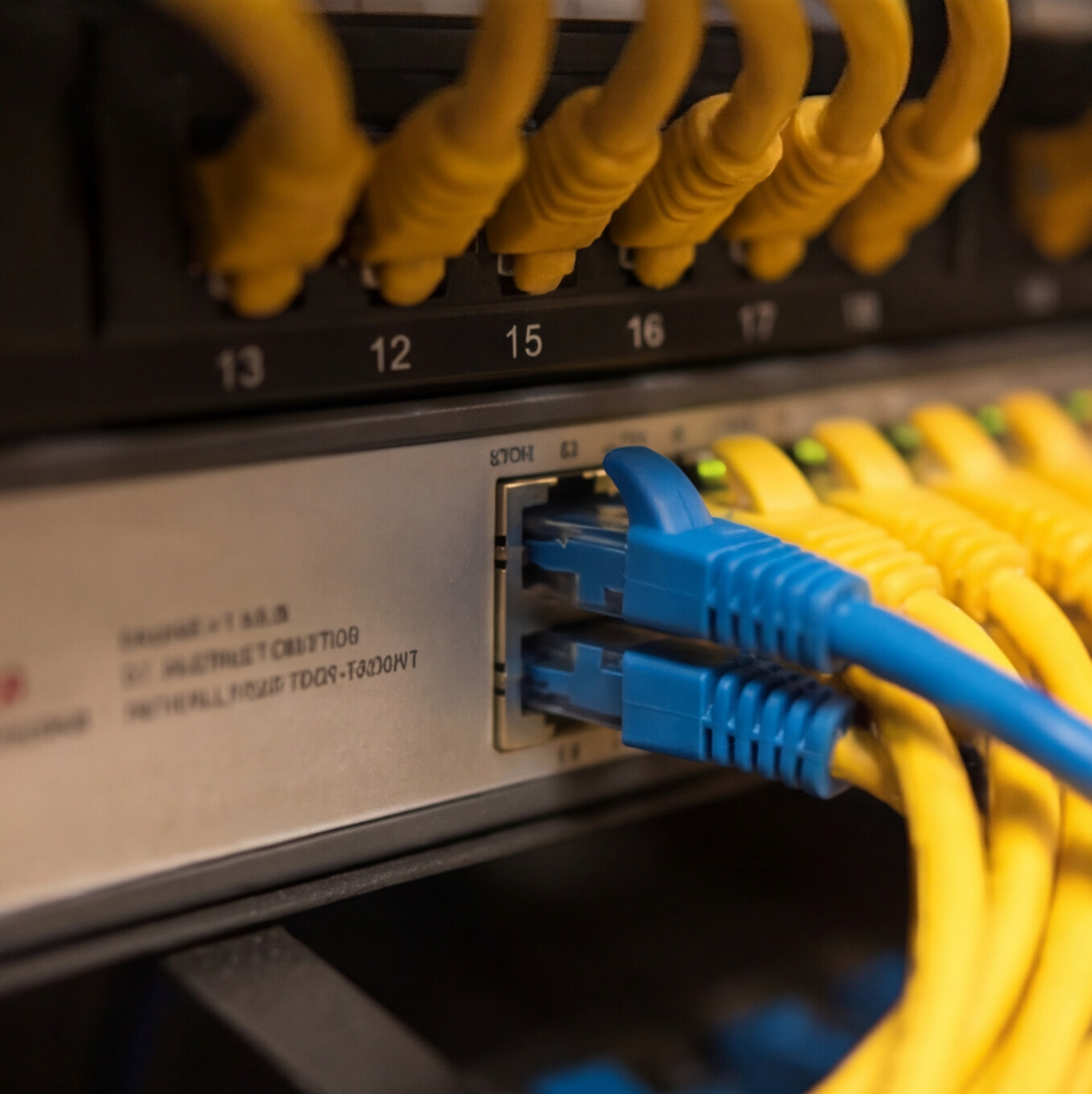 Technician testing network cables in a server rack with a yellow cable tester