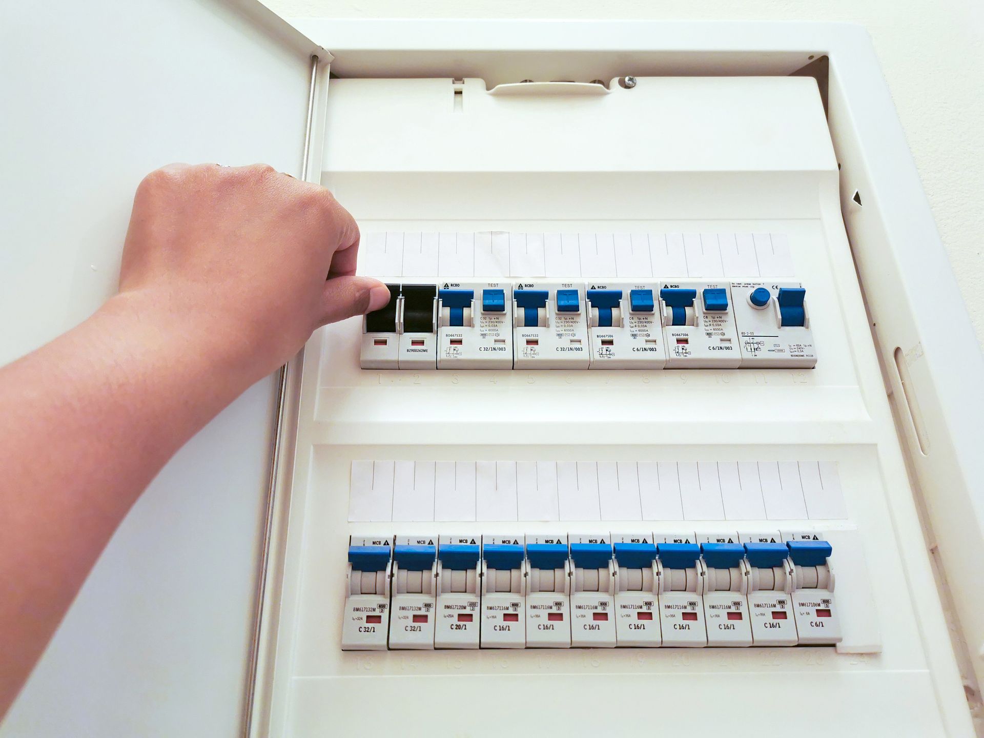 Hand opening an electrical breaker panel with rows of blue switches on white circuit breakers