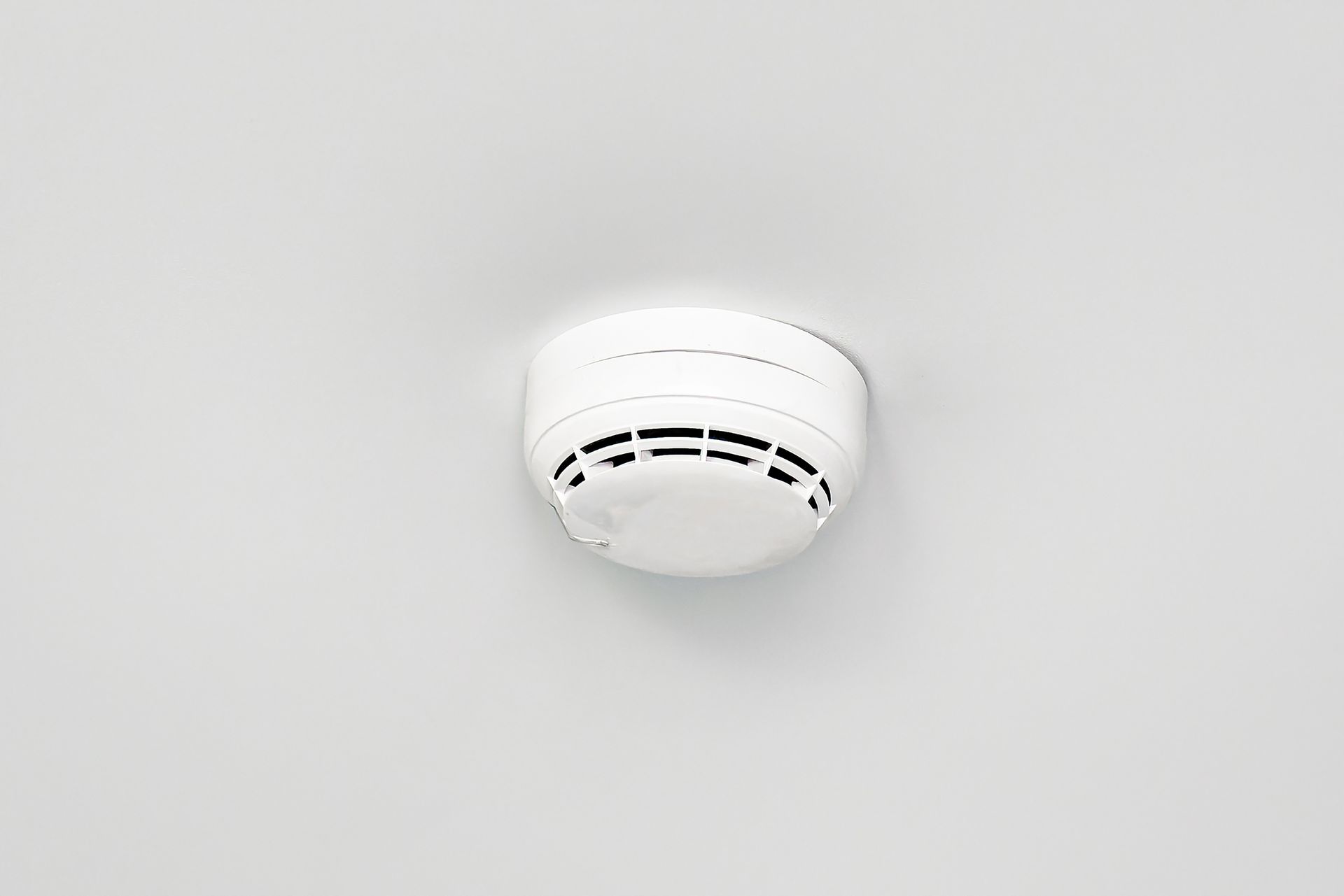 White ceiling smoke detector mounted on a plain light gray ceiling