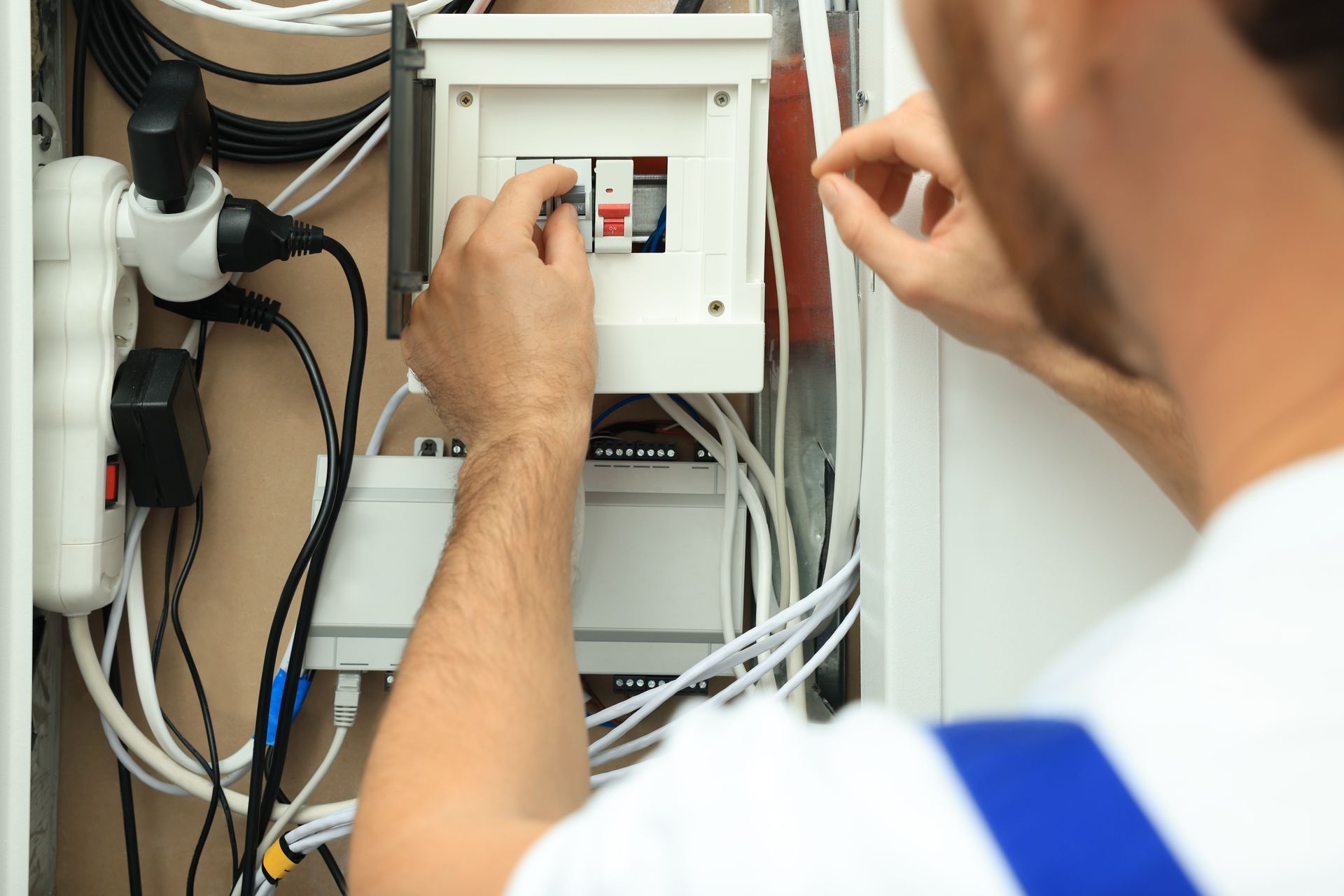 Technician adjusting electrical breakers in an open control panel with exposed wires