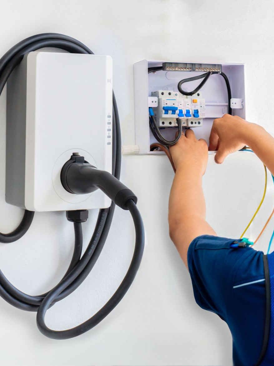 Electric vehicle charger being wired in an open wall box by a technician’s hands