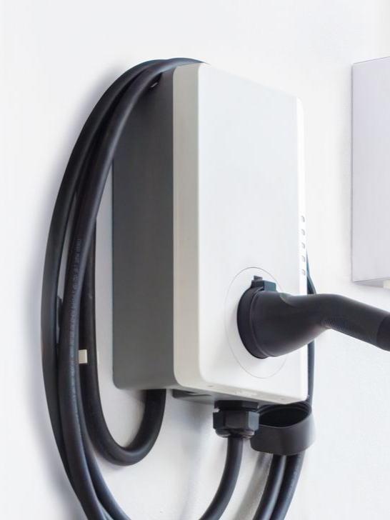 Wall-mounted electric vehicle charger with a black charging cable plugged in
