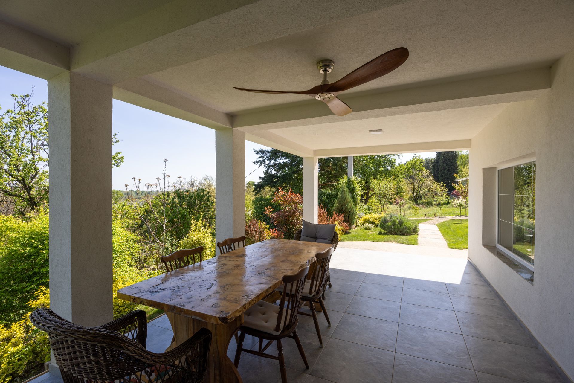 Covered patio with dining table, chairs, and ceiling fan overlooking a sunny garden