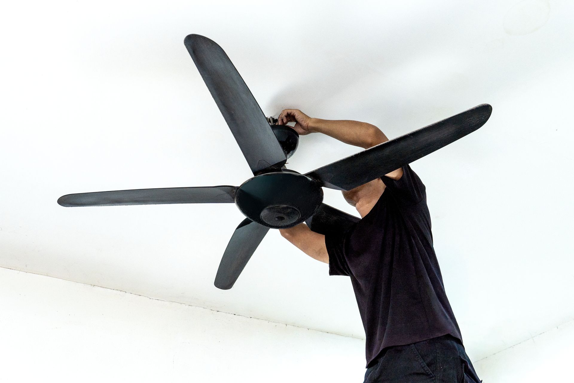 Person installing a black ceiling fan on a white ceiling