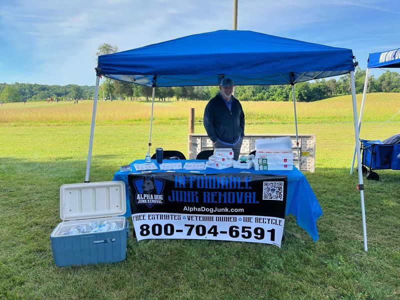 Blue tented outdoor booth with a table, cooler, and sign reading “B&T Towing” and phone number 800-704-6591