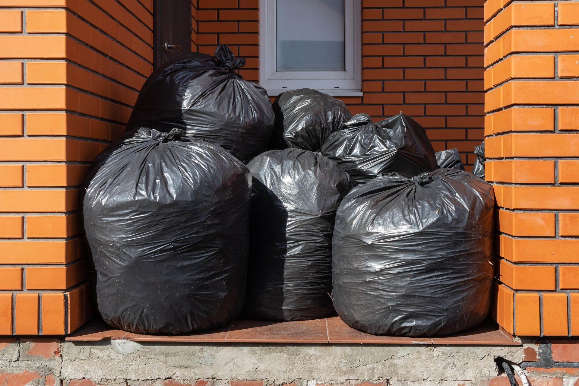Several black garbage bags stacked in a brick doorway