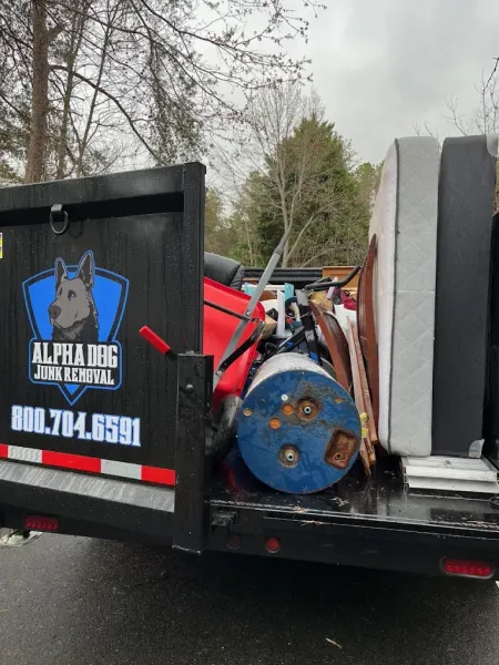 Dump truck bed loaded with red and blue scrap metal beside a wooded roadside.