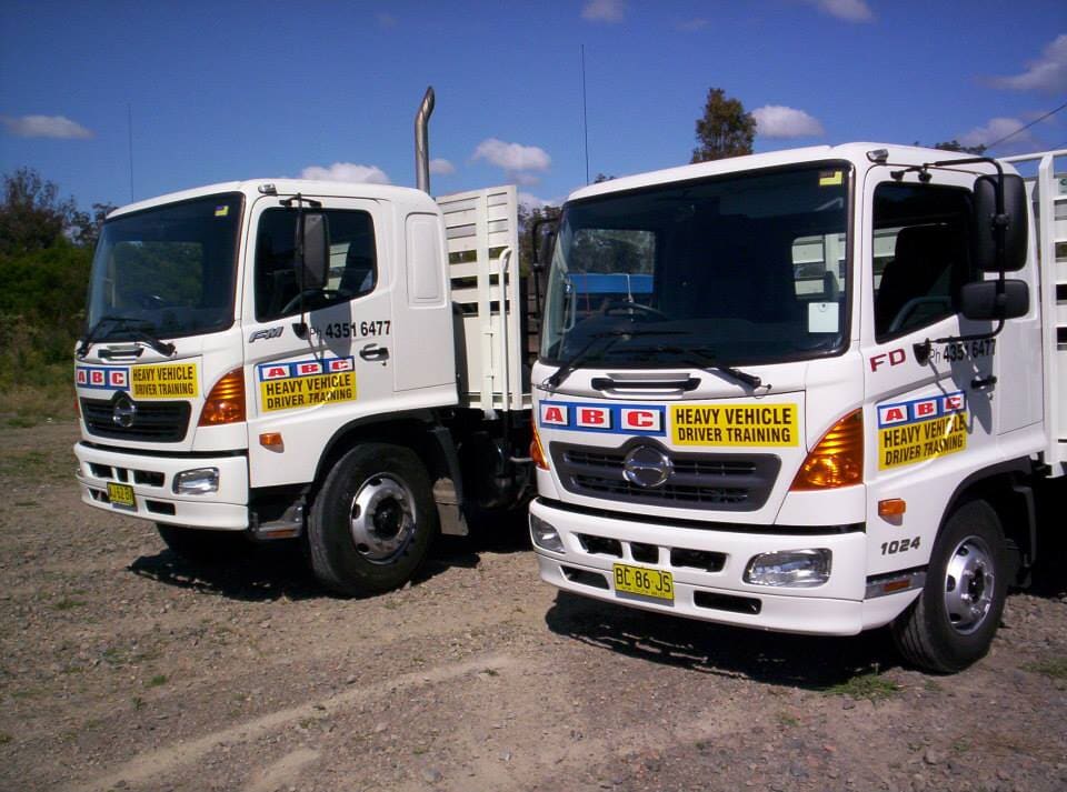 Two White Trucks Are Parked Next To Each Other In A Dirt Field — ABC Driving School Central Coast In Umina Beach, NSW