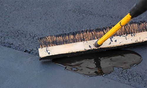 Brush spreading black sealant on a dark surface.