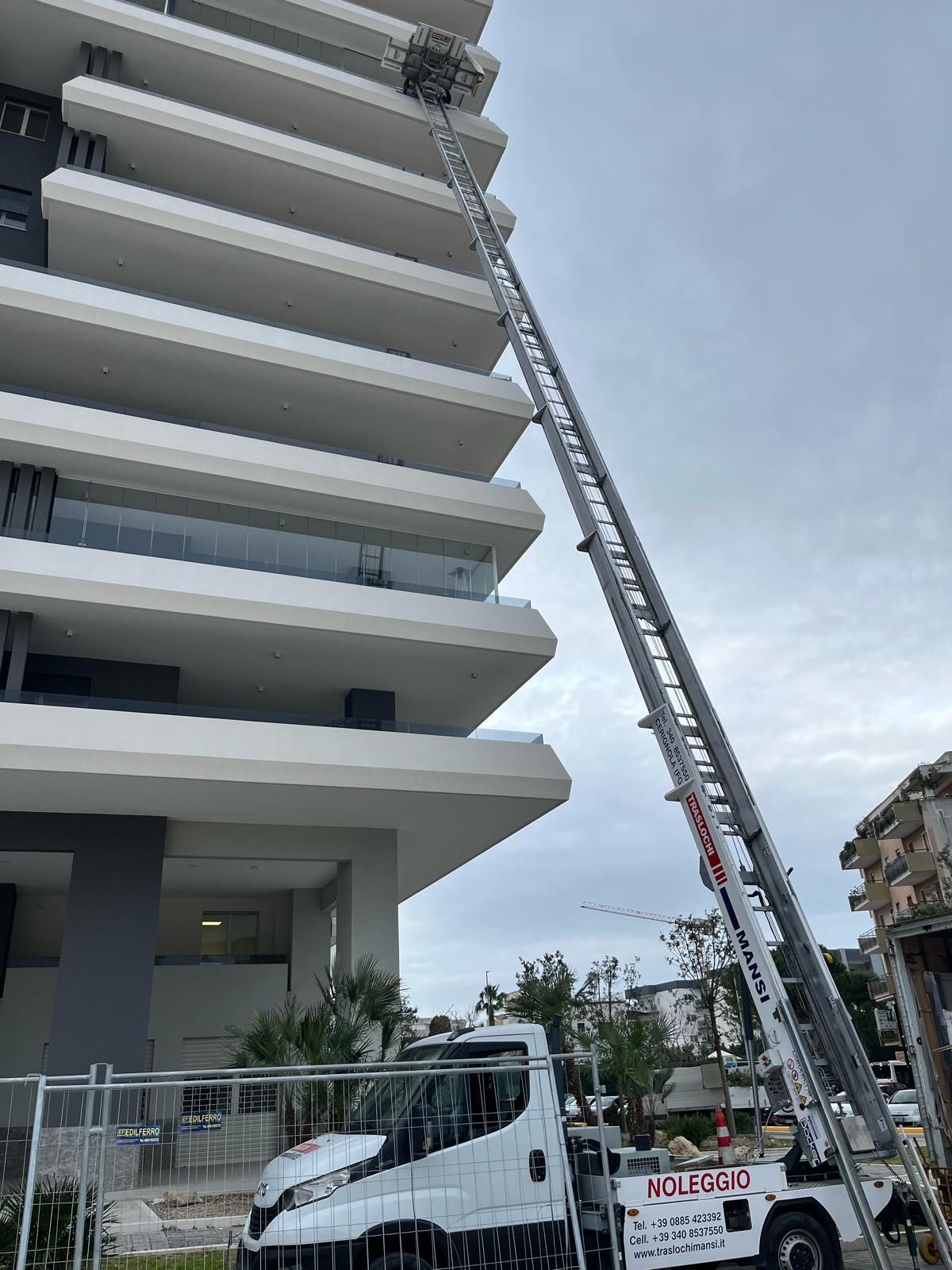 un grosso camion bianco con una scala attaccata è parcheggiato davanti a un alto edificio.