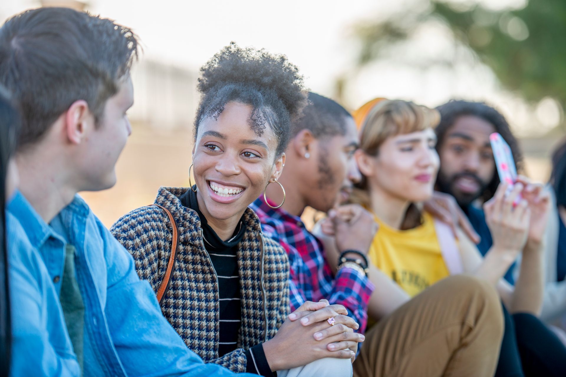 A group of young people are sitting on the ground talking to each other.