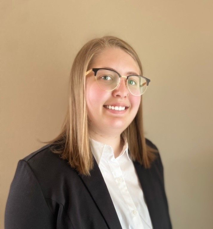 Smiling person in glasses and a black blazer against a plain beige background