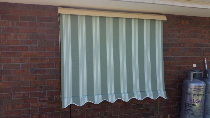 A Green and White Striped Awning is Hanging on a Brick Wall — BTS Blinds & Awnings in Moree, NSW