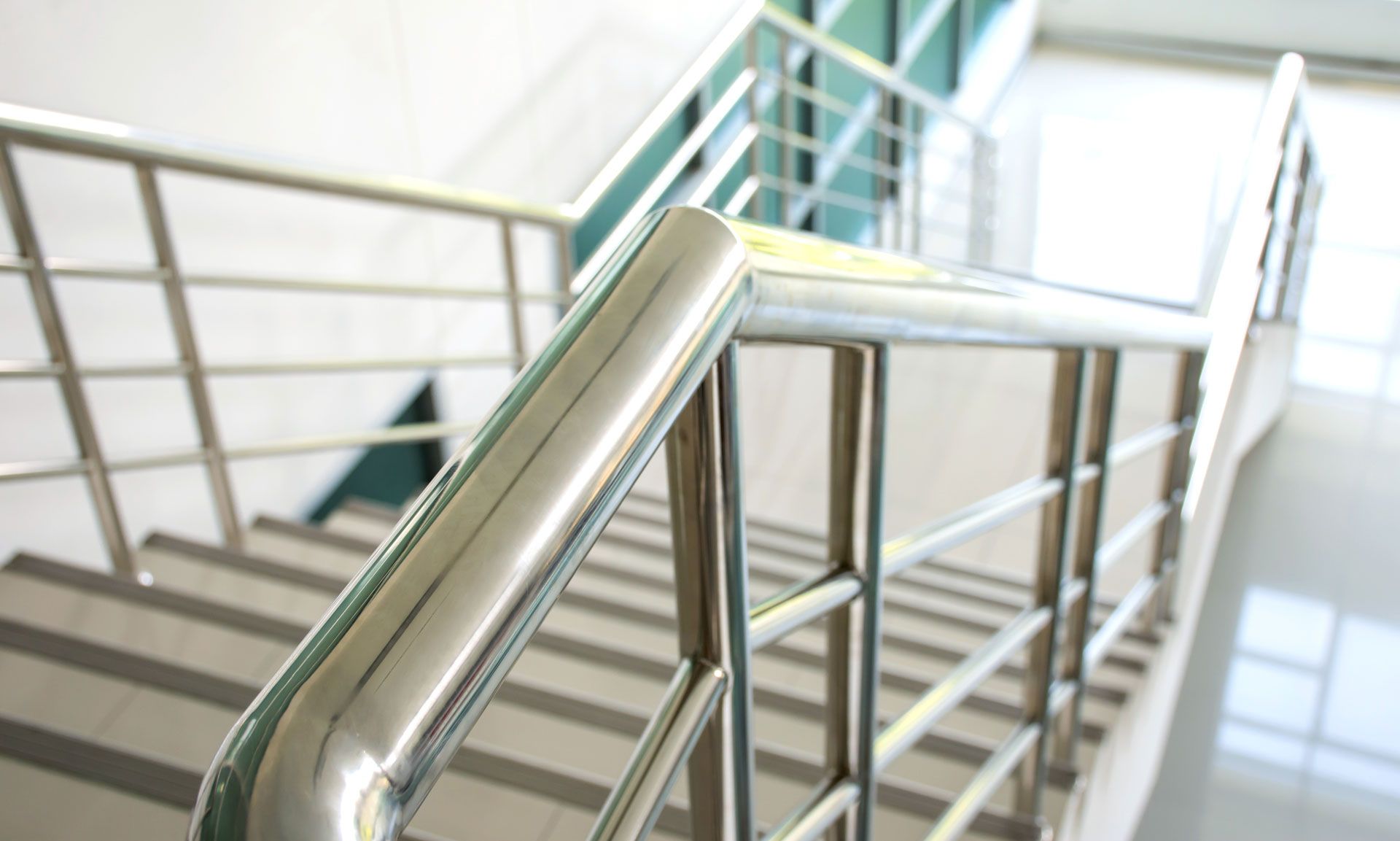 Stainless steel stair railing in a bright indoor stairwell with white walls and steps