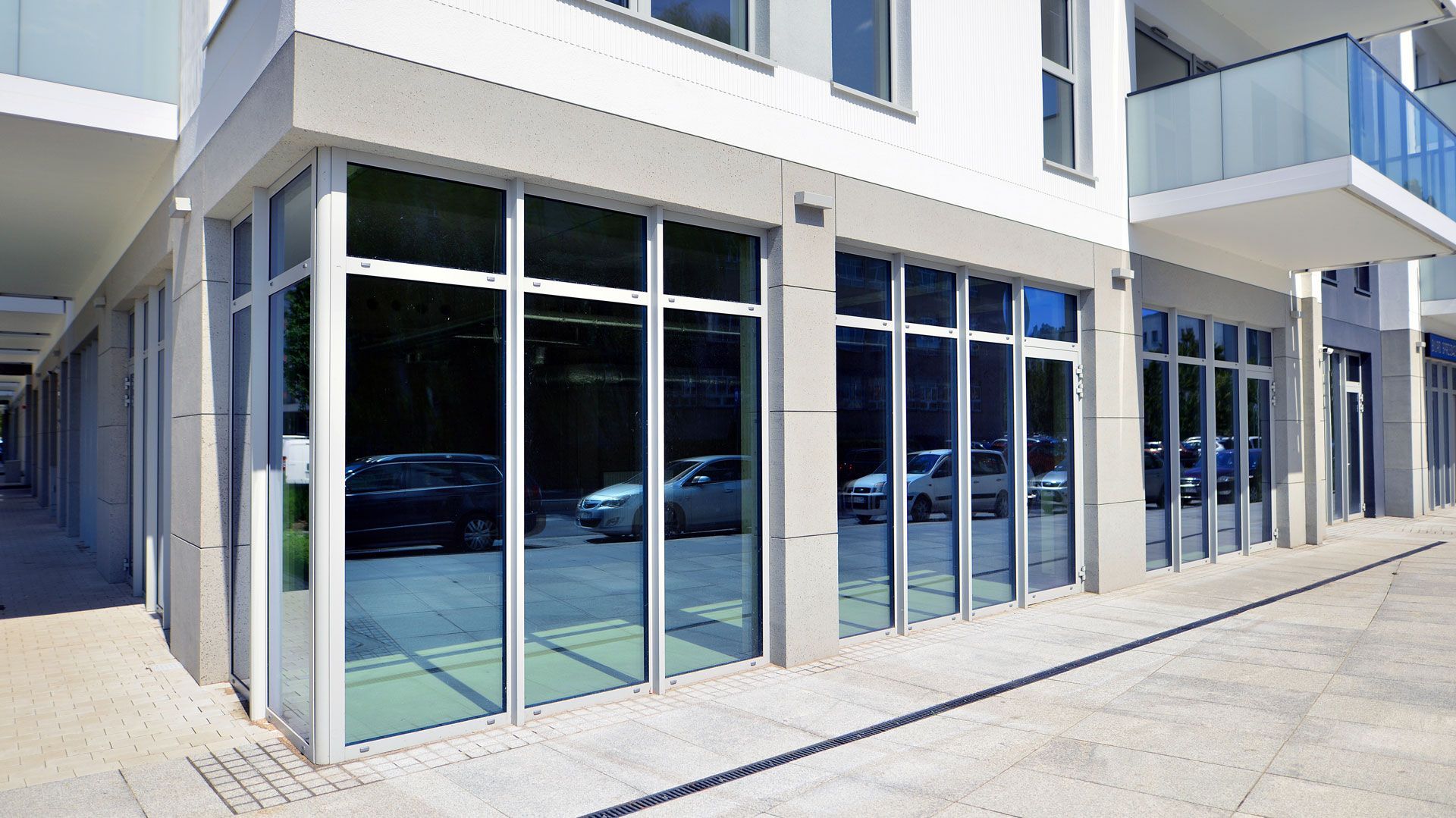 Modern storefront with large glass windows and a white exterior on a sunny sidewalk