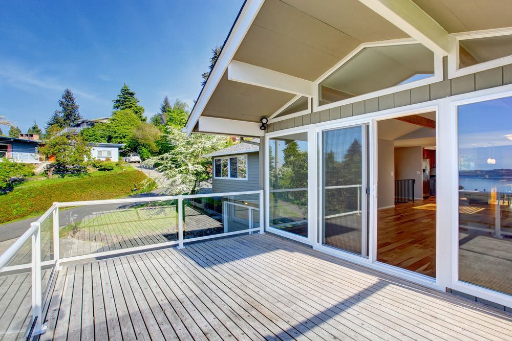 Deck with glass railings and sliding glass doors; view of waterfront homes.