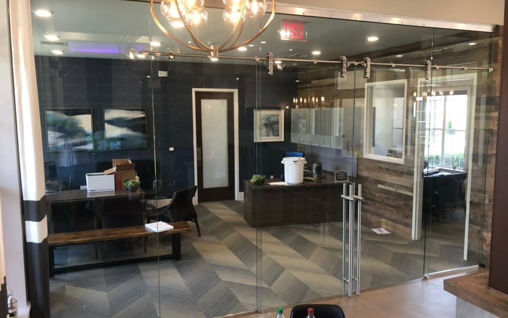 Modern office lobby with glass doors, dark walls, seating, and a geometric rug