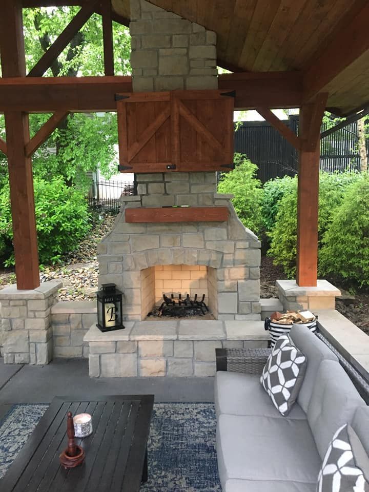 Stone fireplace with wooden accents on a patio with outdoor seating.