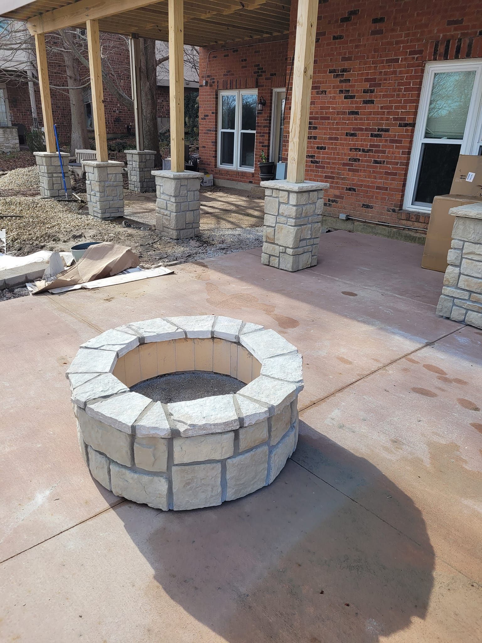 Stone fire pit on concrete patio, under a brick house with a covered wooden porch.