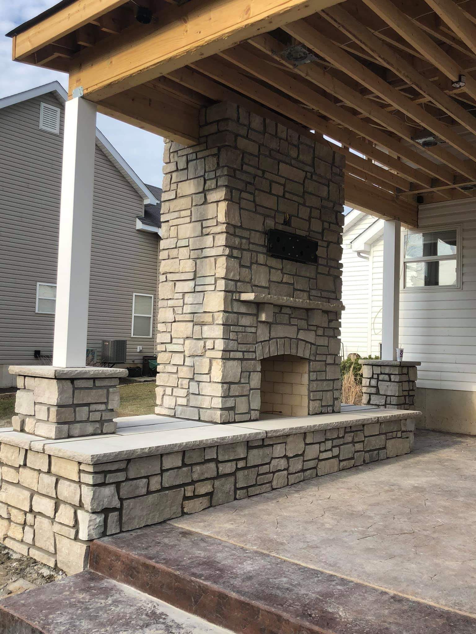Outdoor stone fireplace on a patio with a covered porch overhead.